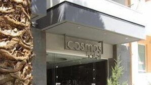 Lasiseinällä varustettu sisäänkäynti ja sen yläpuolella kyltti, jossa lukee ”Cosmos Hotel”.