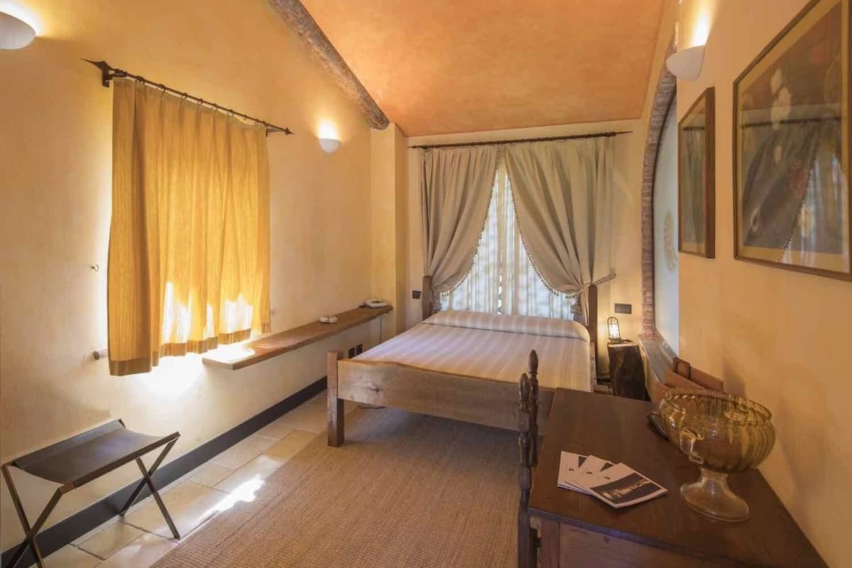 A bedroom with a bed, bedside table, and a small desk with a lamp.