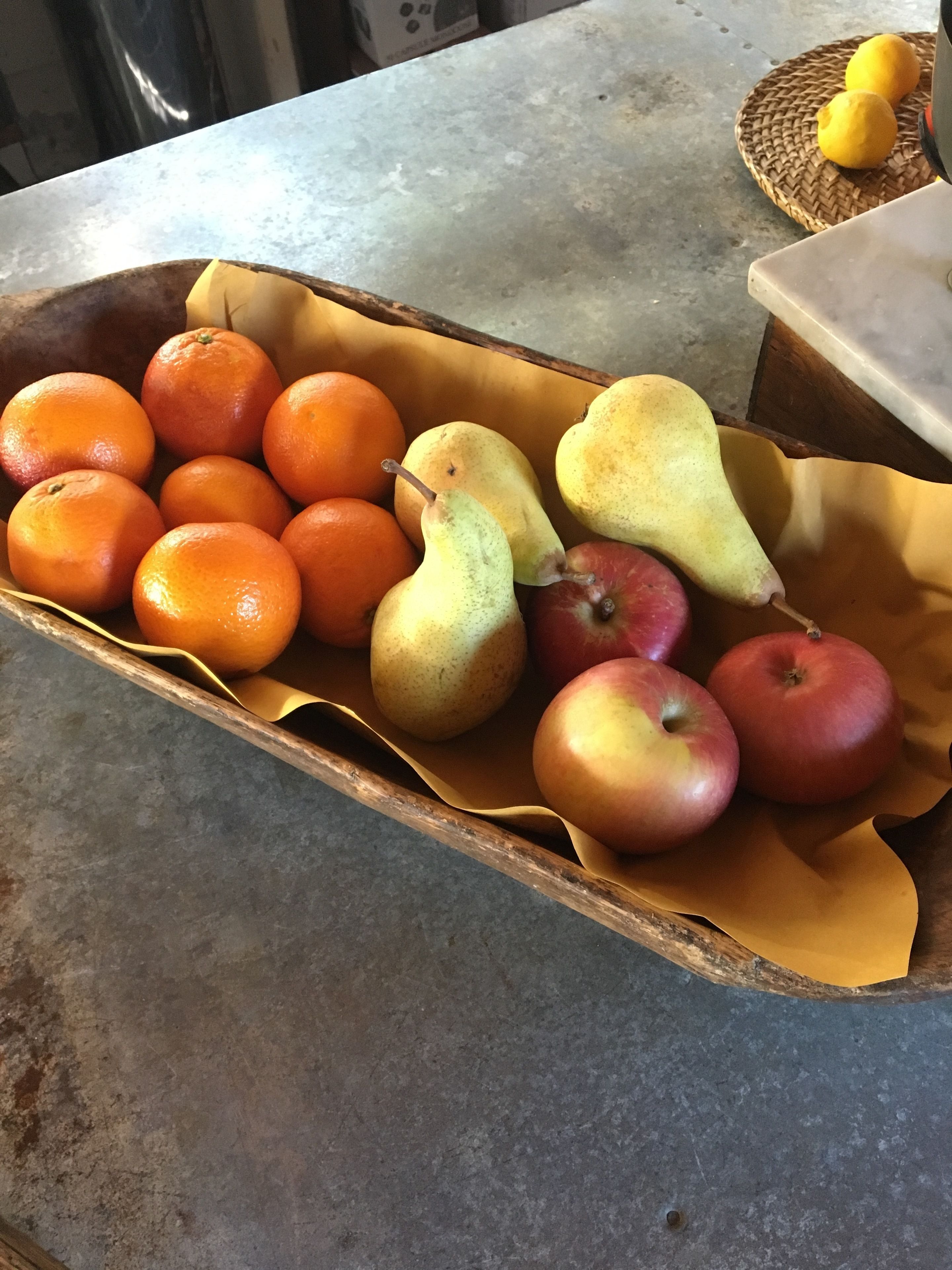 A fruit basket containing oranges, pears, and apples on a table.