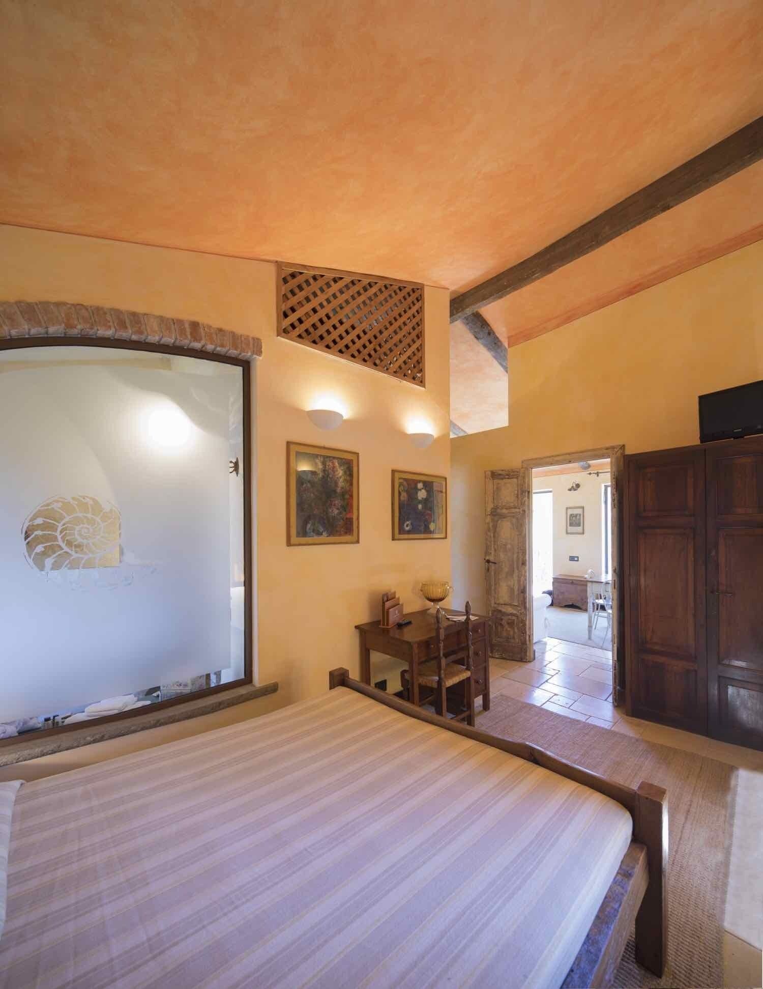 Une chambre à coucher avec un lit, un bureau en bois et une chaise. Les murs sont ornés de tableaux encadrés et il y a un meuble en bois.