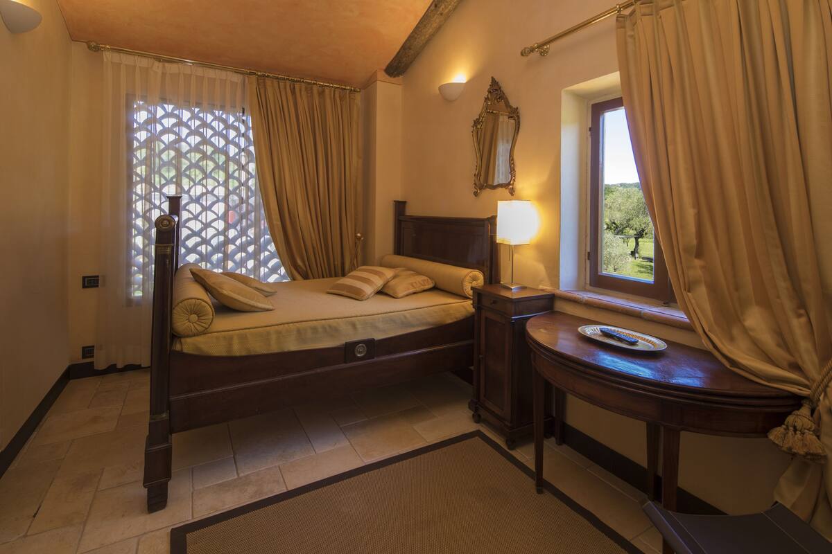 A bedroom with a wooden bed, a bedside table, a lamp, and a window with curtains.