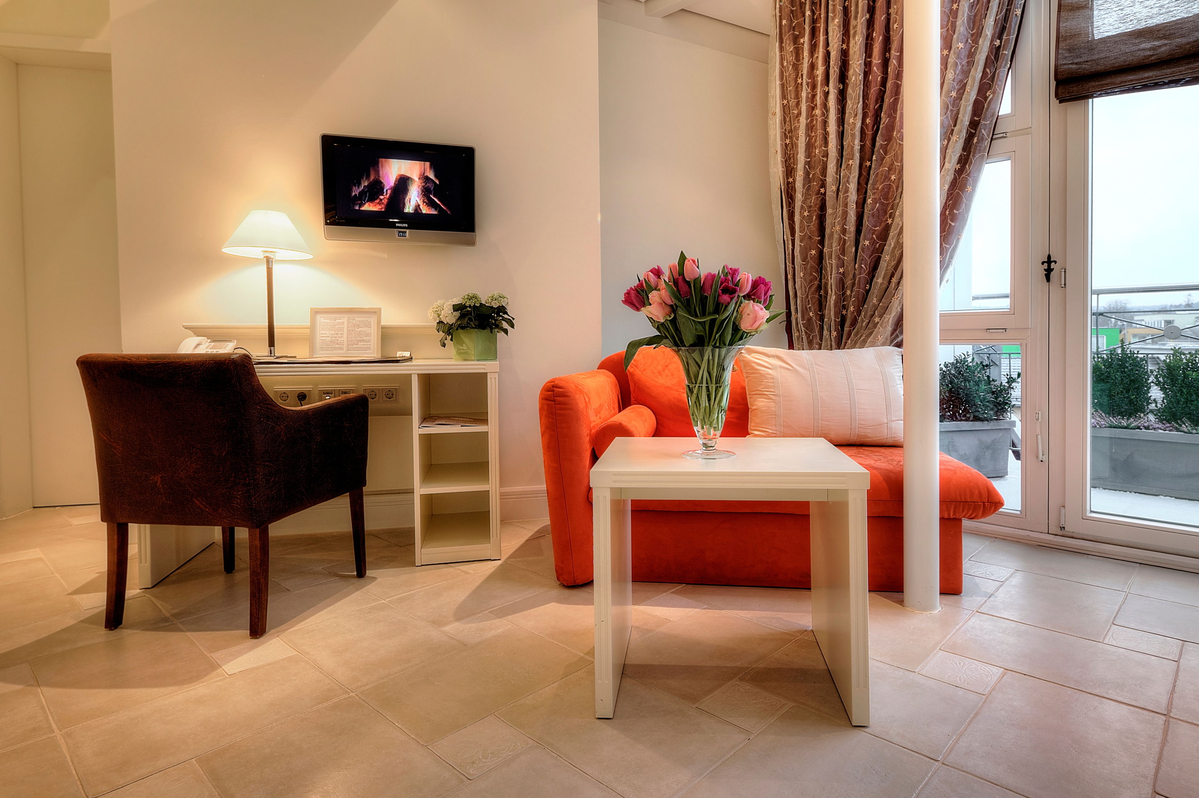A modern living room with a sofa, a small table, a chair, a TV, and a window with curtains.