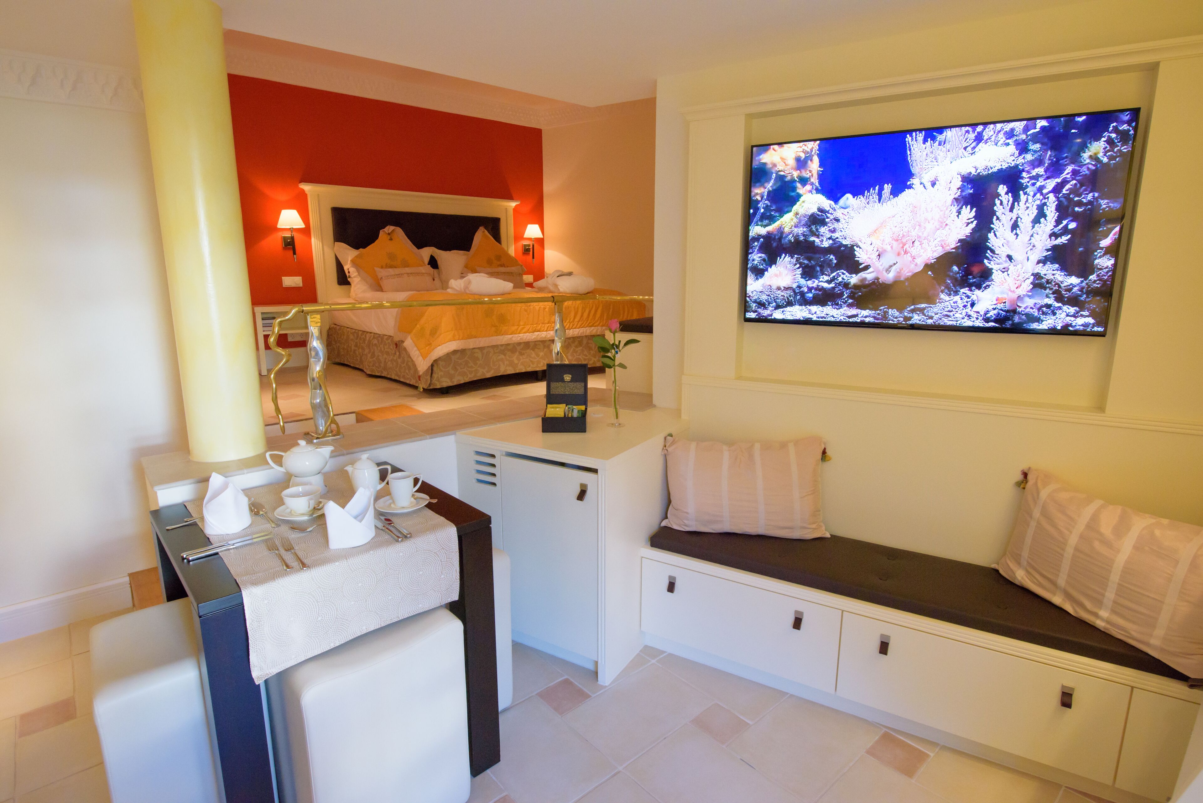A hotel room with a bed, a TV, a desk with a tea set, and a seating area.