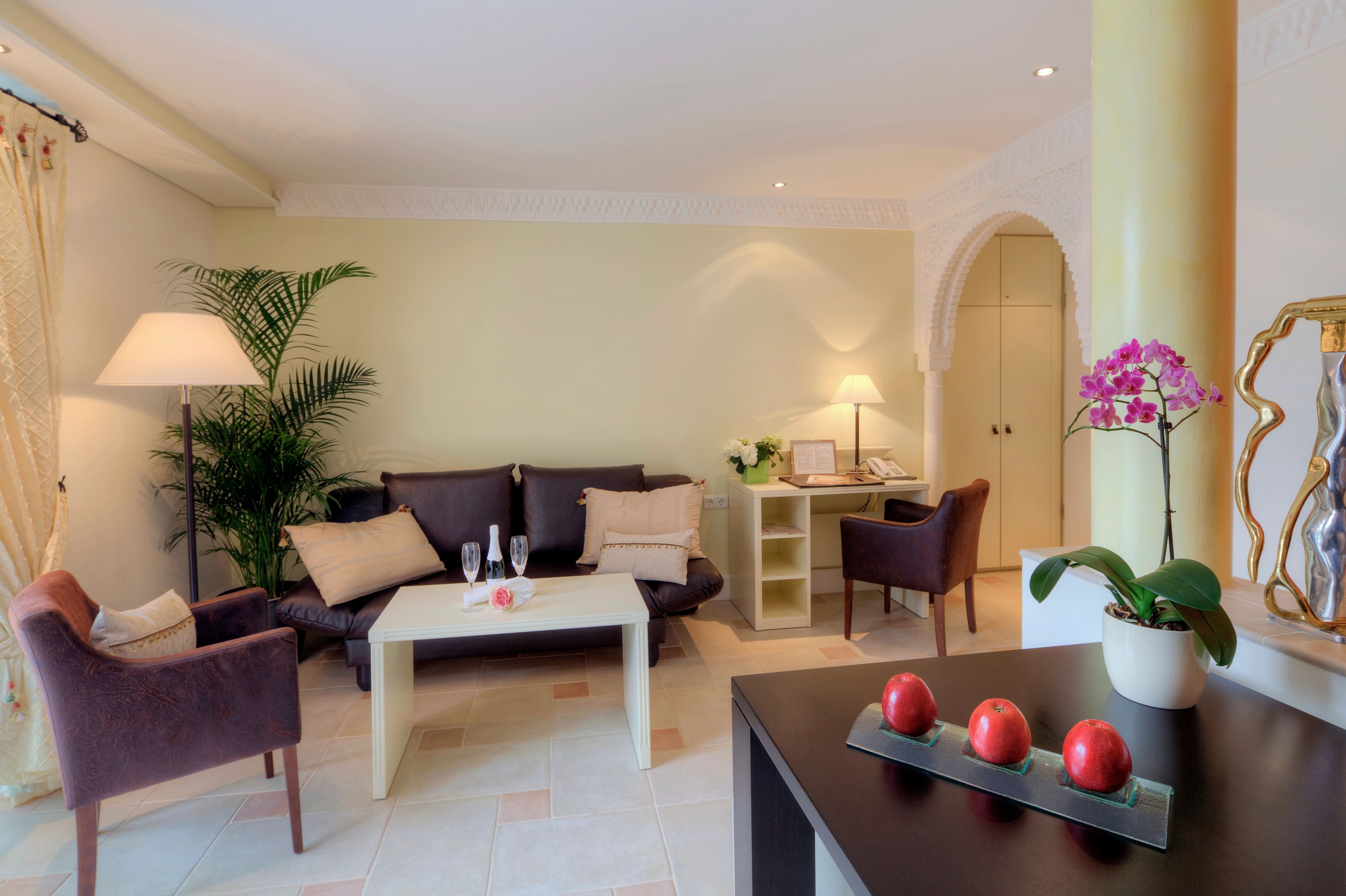 A modern living room with a sofa, armchairs, a coffee table, and a dining table. There is a potted plant and a vase with flowers on the dining table.