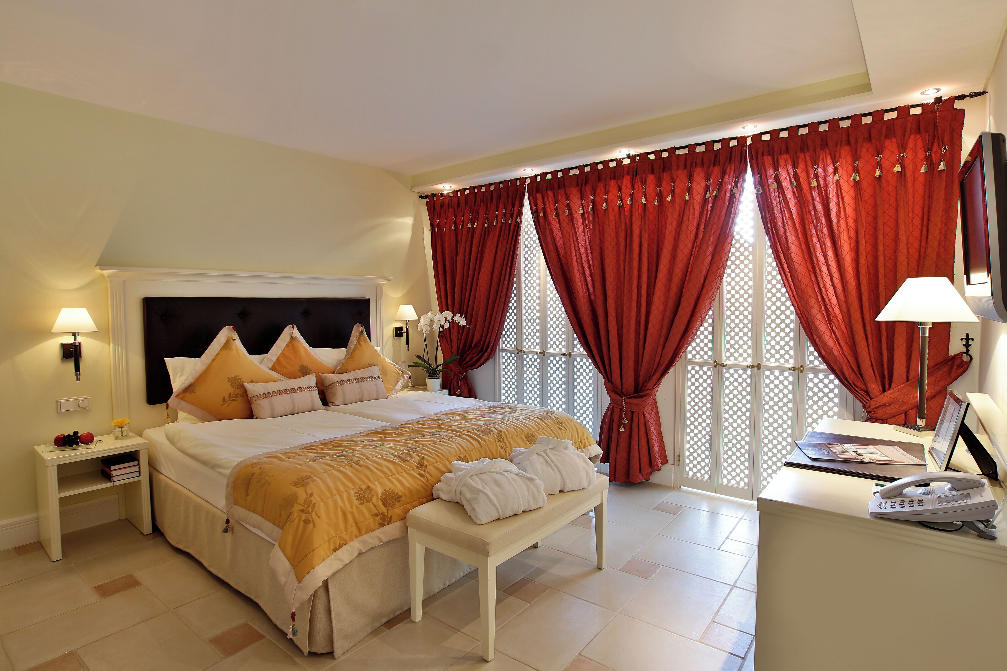 Un dormitorio ordenado con cama, mesitas de noche, escritorio y teléfono.