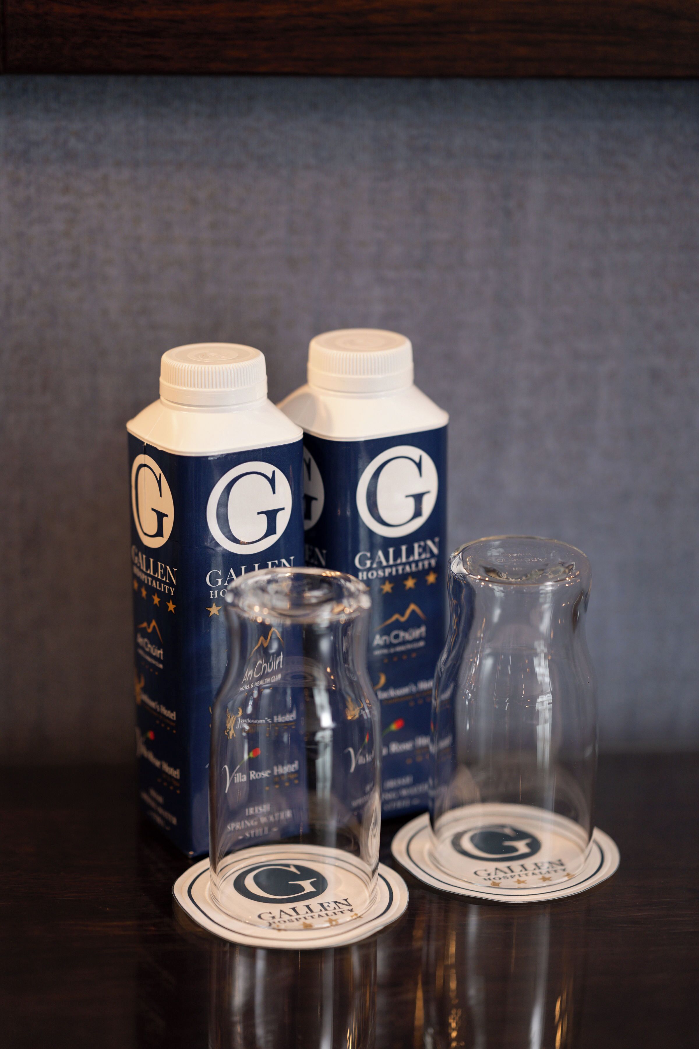 Two Gallen Hospitality branded bottles and two coasters with the hotel's logo.