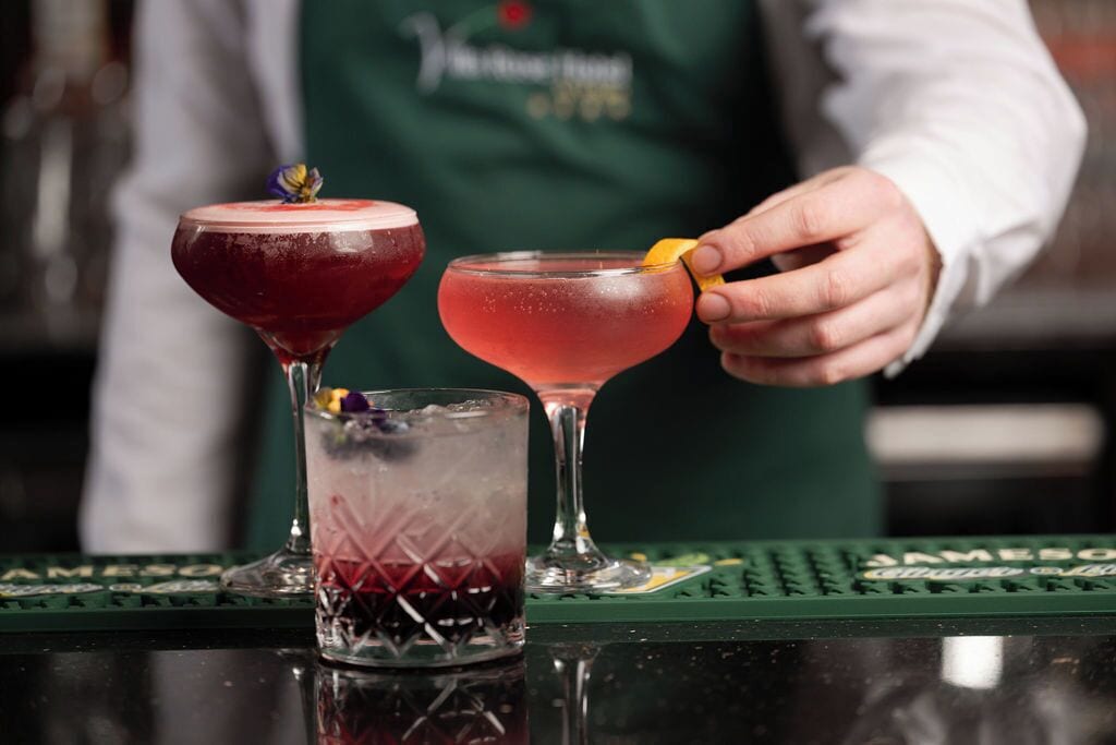 Ein Barkeeper bereitet Getränke an der Bar zu, mit einer grünen Unterlage und einem beschrifteten Untersetzer.