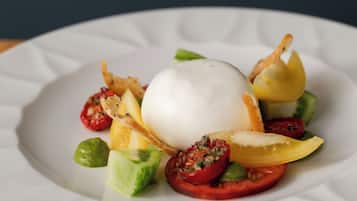 A white plate with a white spherical food item surrounded by sliced vegetables and a small piece of fried food.