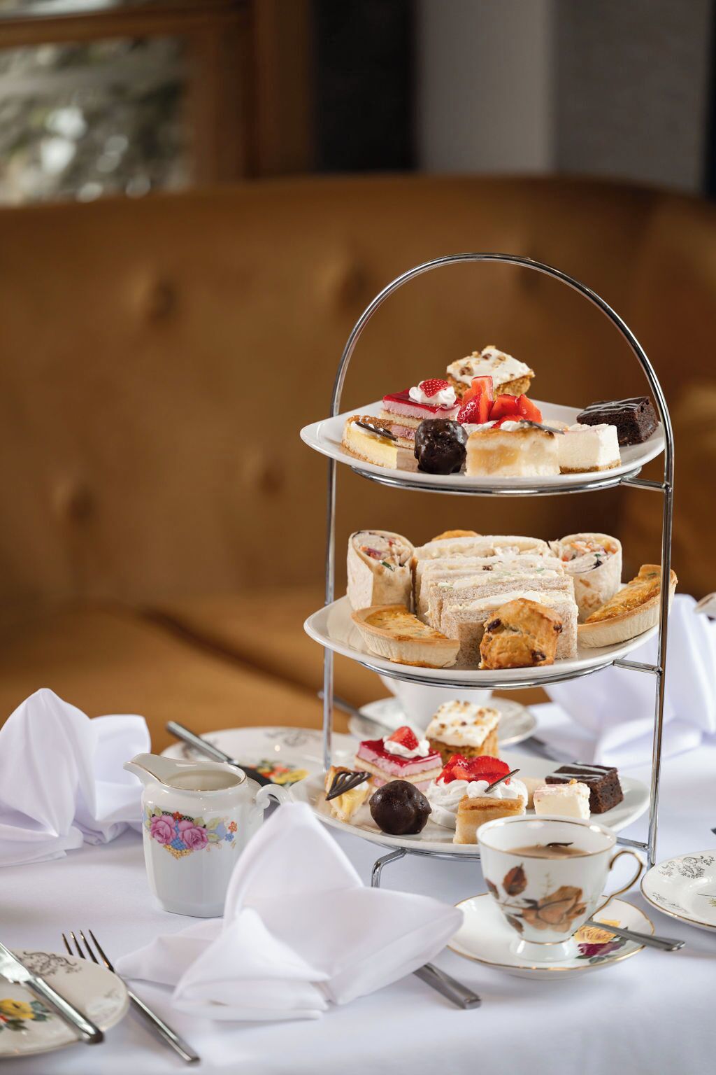 A three-tiered dessert stand with various pastries and cakes, accompanied by tea cups and saucers on a table.