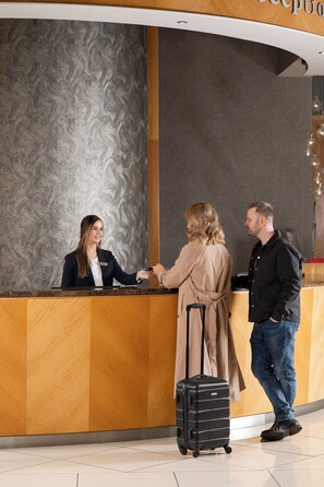 A reception desk with a receptionist, a guest, and a man with a suitcase. - Villa Rose Hotel & Spa (Ballybofey)