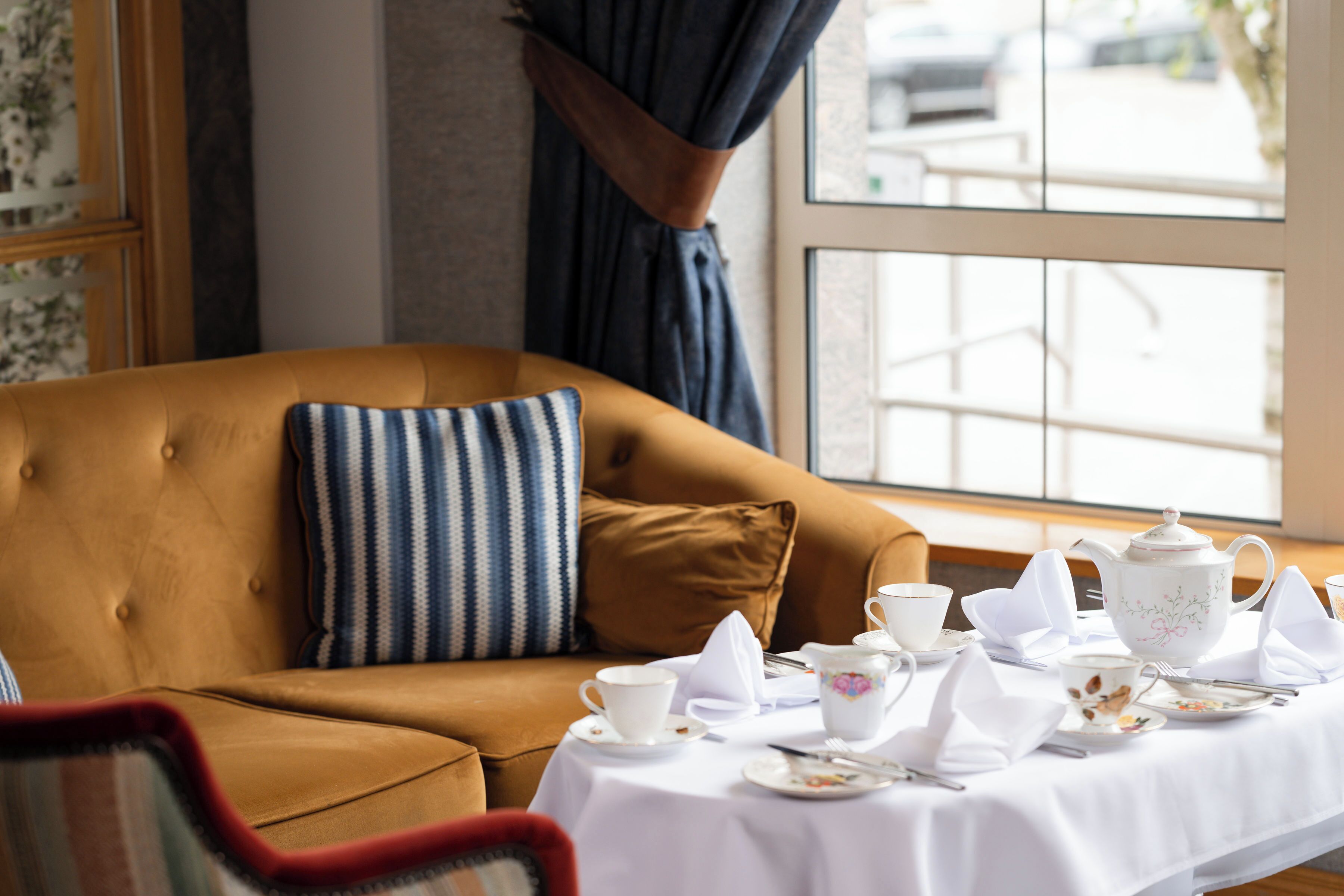 A cozy room with a brown sofa, a striped pillow, and a table set for tea with white tablecloth and tea cups.
