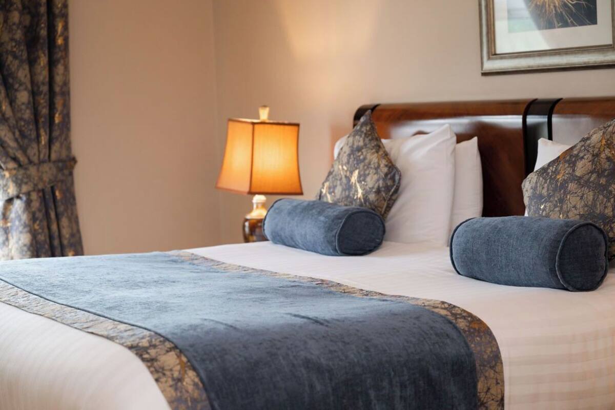 A hotel room with a bed, pillows, a lamp, and a framed picture on the wall.