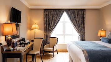 Una habitación de hotel con una cama, un escritorio con lámpara, una silla, un televisor y una ventana con cortinas.