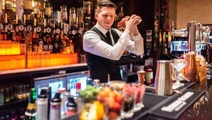 Un bar con un cantinero preparando bebidas, estantes llenos de botellas de licor y una variedad de utensilios e ingredientes para coctelería.