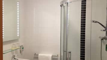 A bathroom with a glass shower enclosure, a sink, and a mirror with lights.