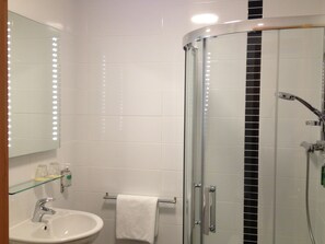 A bathroom with a glass shower enclosure, a sink, and a mirror with lights. - Villa Rose Hotel & Spa (Ballybofey)