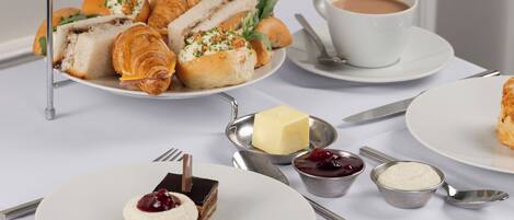 Un présentoir à étages garni de diverses pâtisseries et une tasse de thé, le tout posé sur une table.