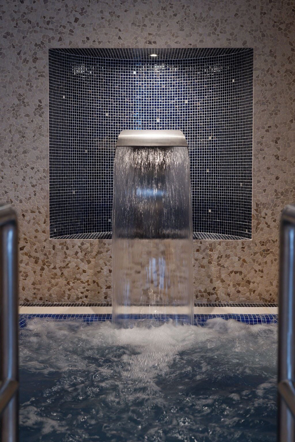 Un jacuzzi con pared de azulejos y barandilla de metal.