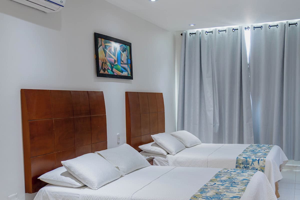 A hotel room with two beds, a wooden headboard, a white table, and a painting on the wall.
