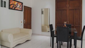 A room with a beige sofa, a dining table with chairs, wooden wardrobes, a large mirror, and a wall-mounted abstract painting. - Hotel Coral Reef Cartagena (Cartagena)