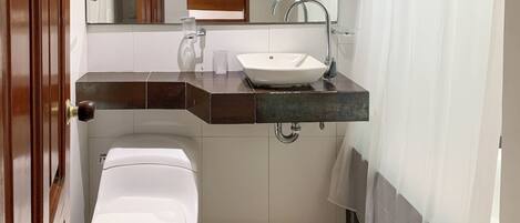 A compact bathroom with a white toilet, a sink with a mirror above, and a shower curtain.