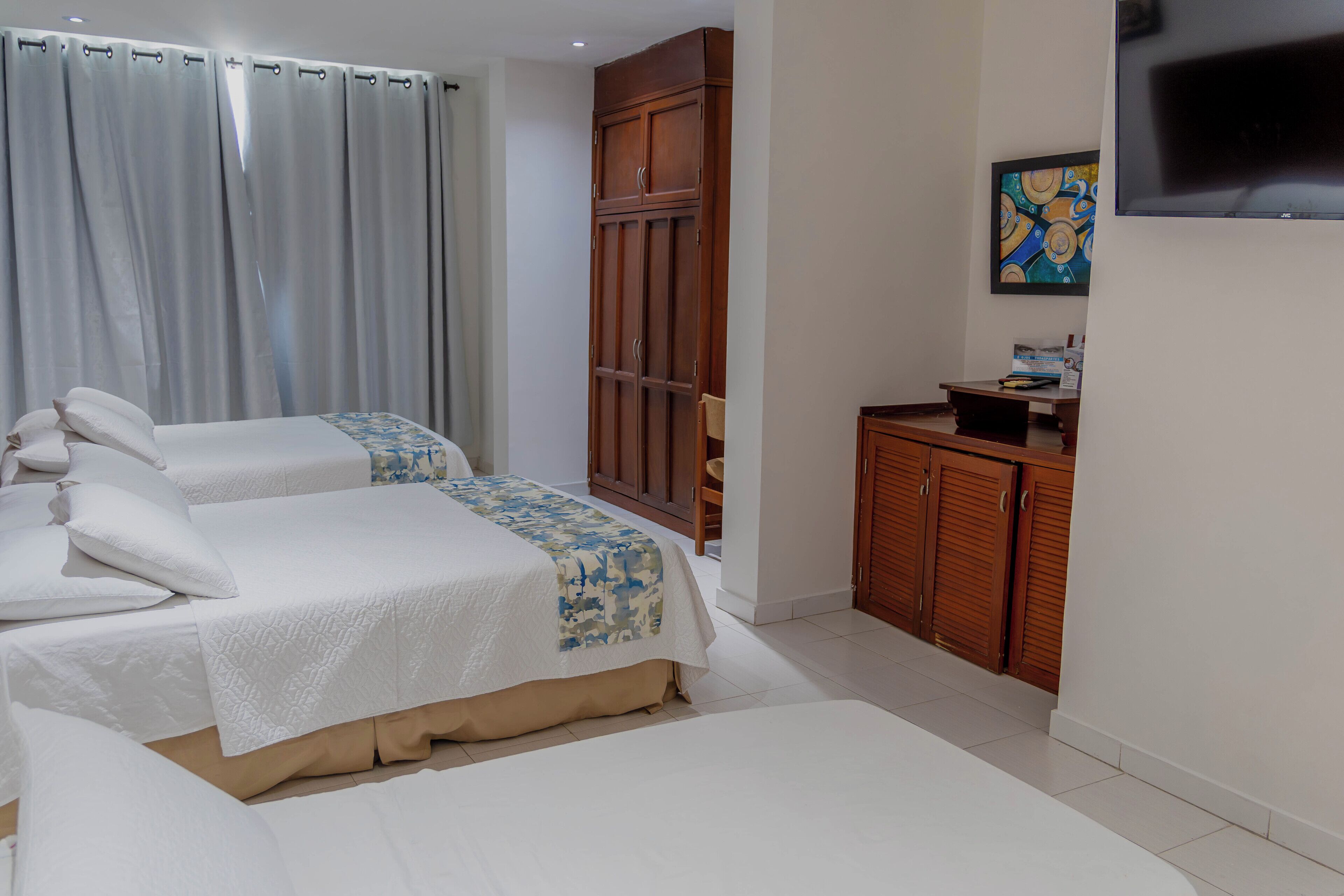 A hotel room with two beds, a wooden wardrobe, a television, and a painting on the wall.