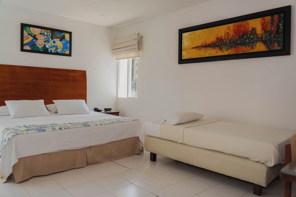 A hotel room with a large bed, a smaller sofa, a nightstand, and two paintings on the walls.