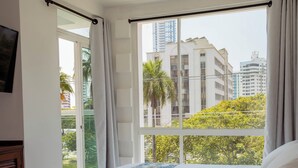 A hotel room with a large bed, a TV mounted on the wall, and a view of the cityscape through the window. - Hotel Coral Reef Cartagena (Cartagena)
