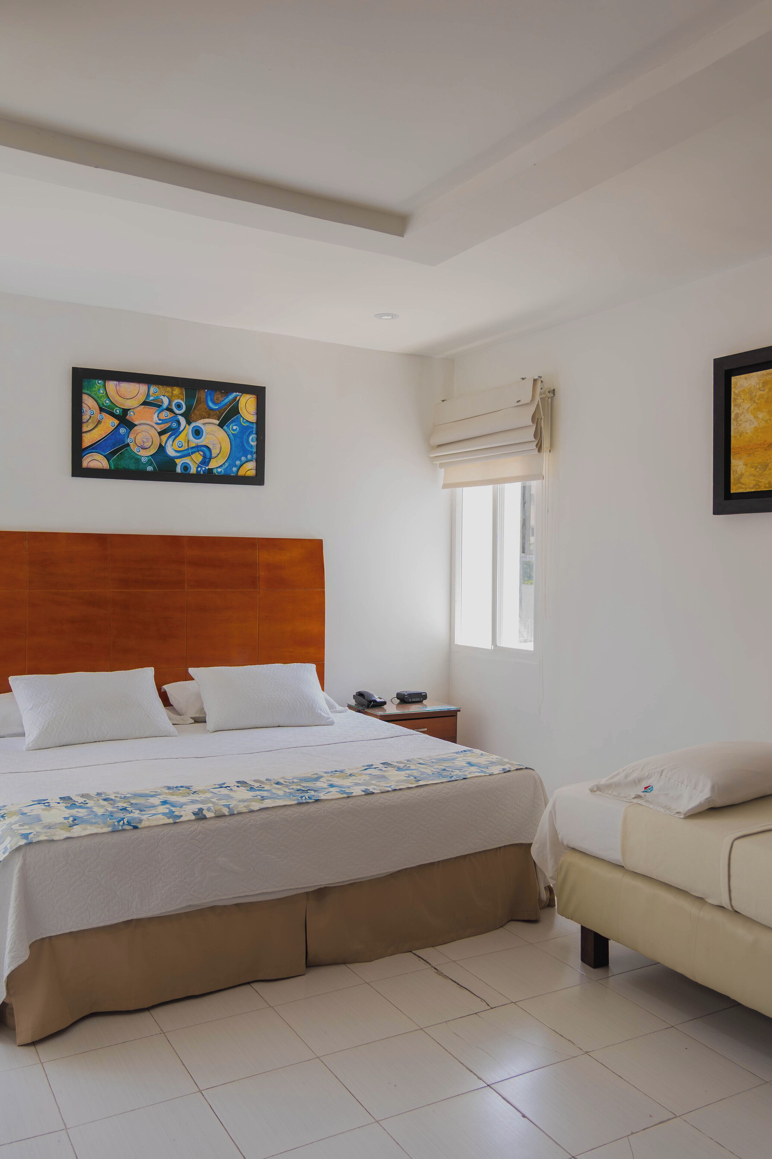 A bedroom with a wooden headboard bed, a bedside table, a window with an air conditioning unit, and a sofa.