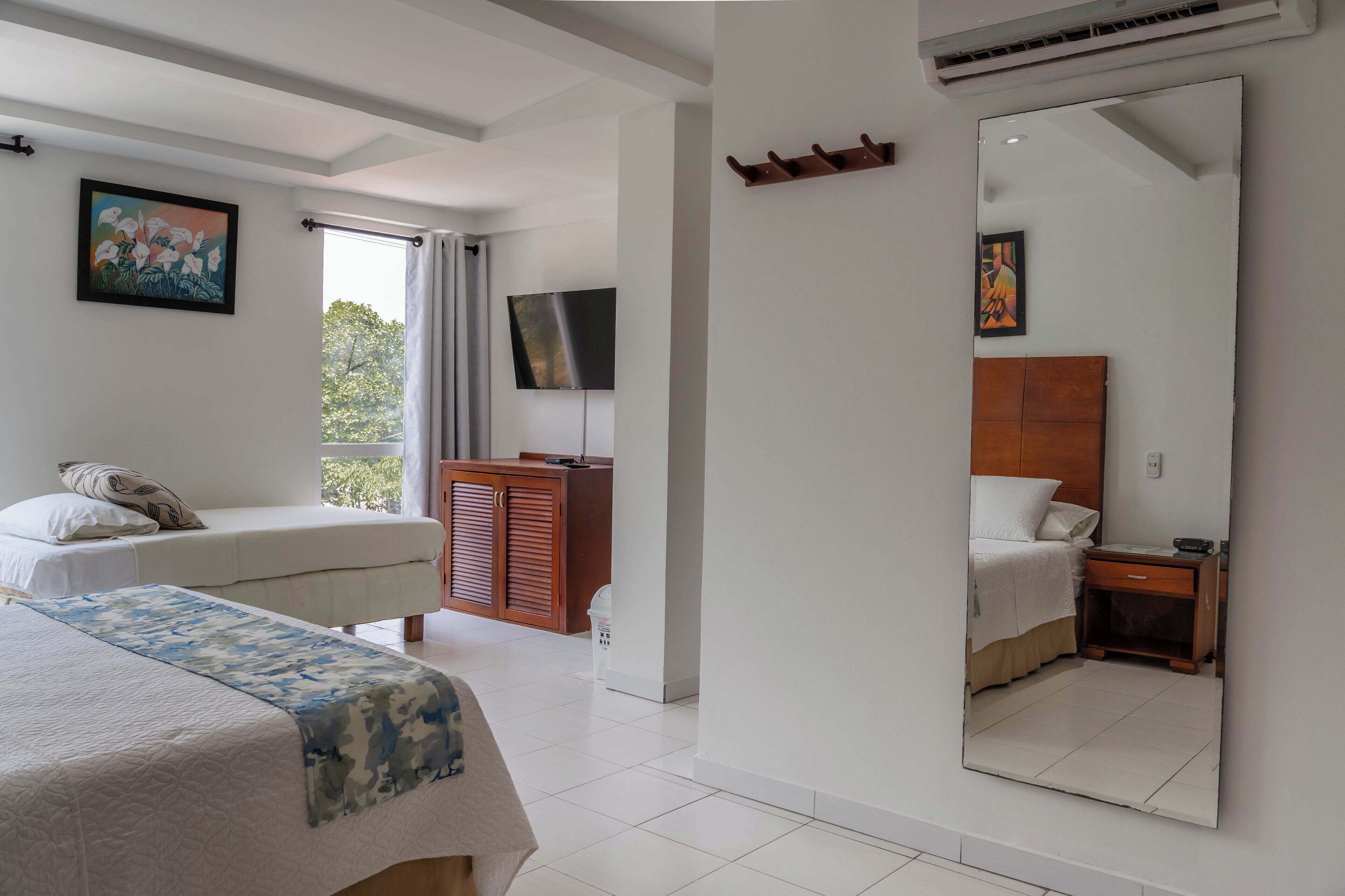 A hotel room with a bed, a bedside table, a TV, a wardrobe, and a large mirror.