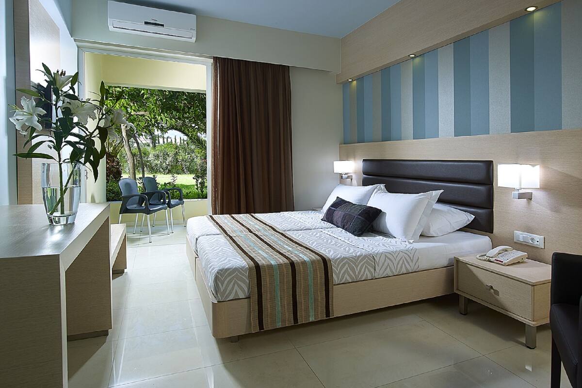 A modern hotel room with a large bed, bedside tables, a desk, and a view of the outdoors.