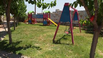 A playground with swings and slides, surrounded by trees and a stone wall.