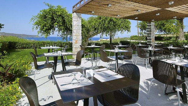 An outdoor dining area with tables and chairs, a wooden pergola, and a view of the sea. - Eleftheria Hotel (Chania)