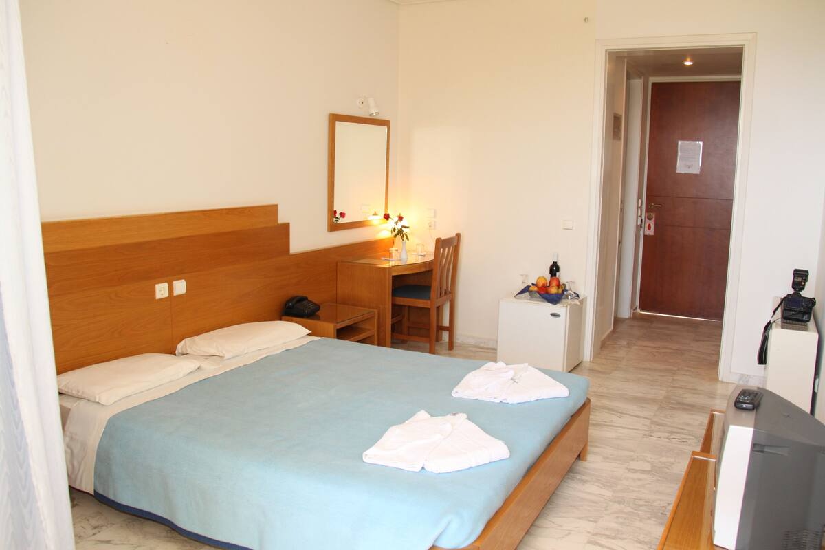 A hotel room with a bed, a desk, a chair, a small cabinet, and a television.