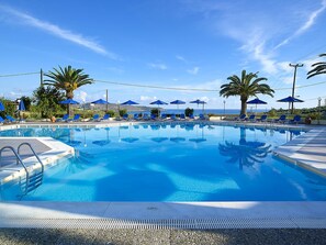 Una piscina azul cristalina con sillas de descanso y sombrillas, rodeada de palmeras y vistas al mar.