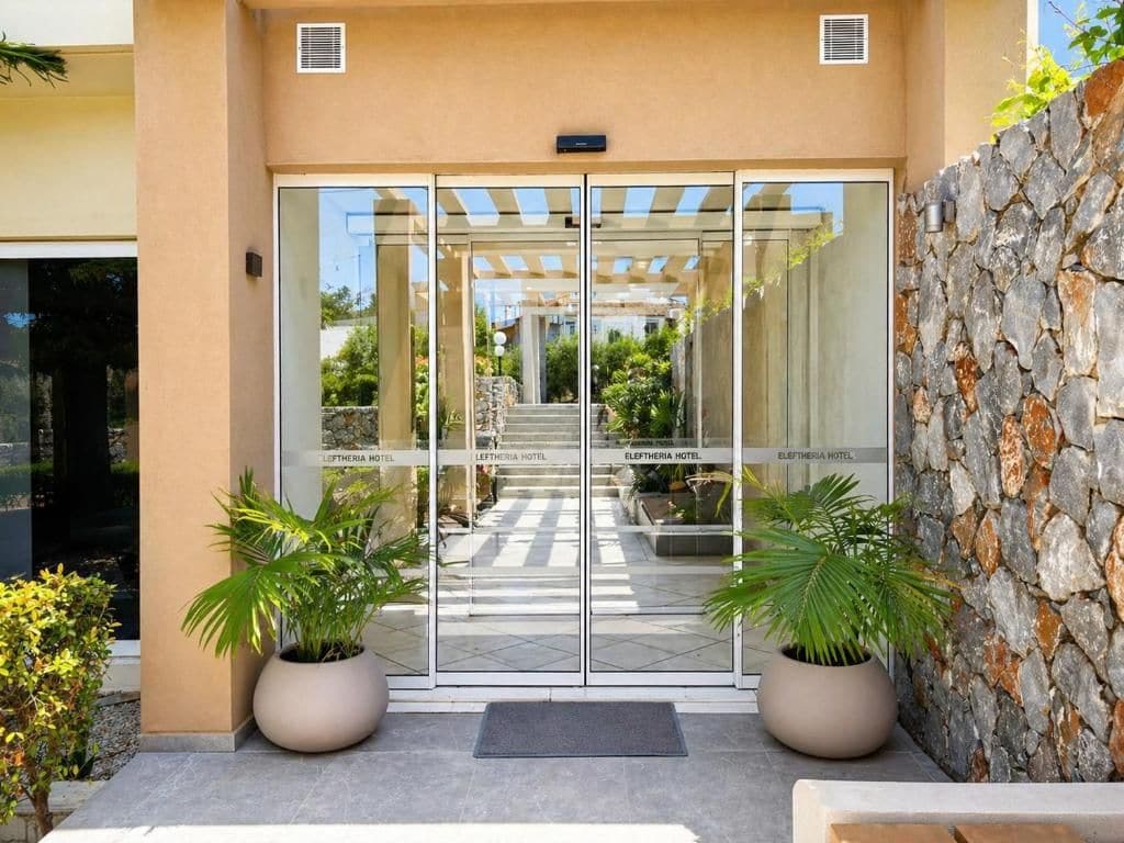 A hotel entrance with a glass door, a stone wall, and potted plants.