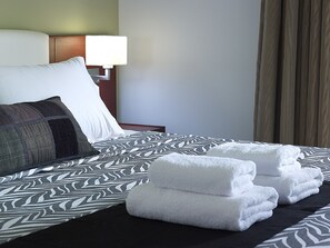 Una cama bien hecha con ropa de cama estampada, una lámpara de noche y toallas dobladas sobre la cama.