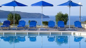 A poolside area with blue lounge chairs and umbrellas, a clear view of the sea, and a calm pool reflecting the surroundings. - Eleftheria Hotel (Chania)