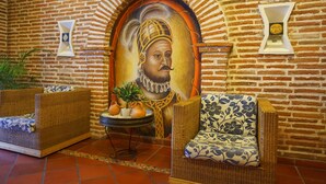 Een kamer met een bakstenen muur, twee rieten banken, een tafel met een plant en een decoratief schilderij.