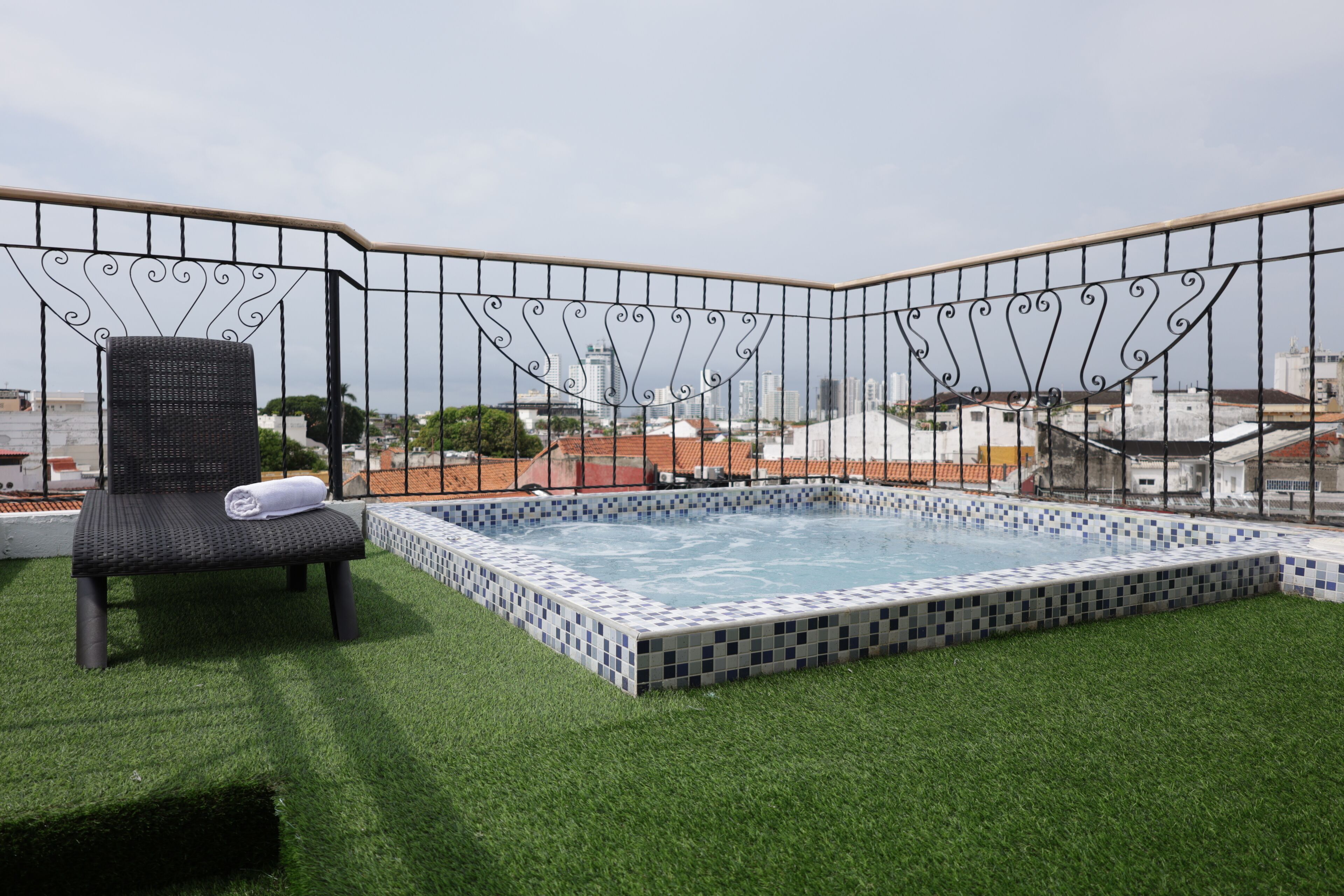 A rooftop pool area with a chair and a small pool, surrounded by a metal fence.