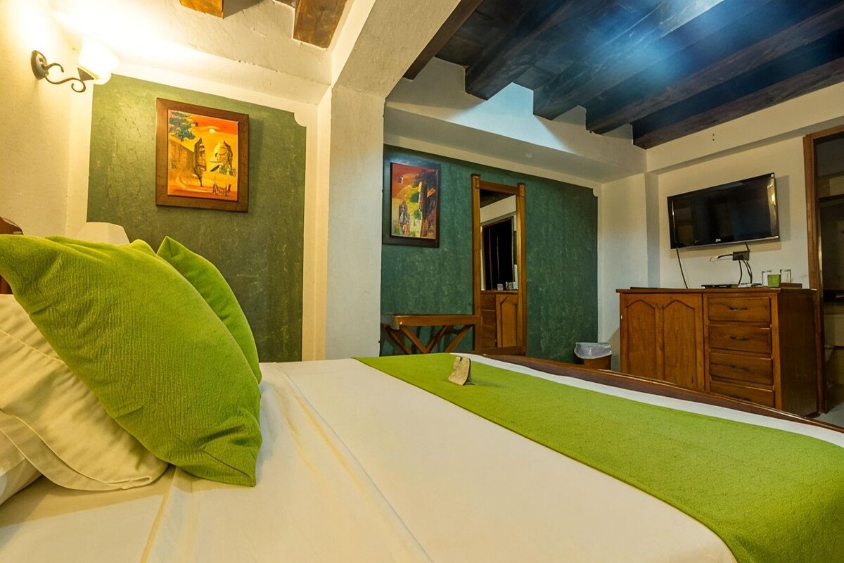 Een kamer met een bed, een houten dressoir, een televisie en twee schilderijen aan de muur.