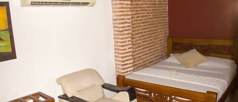 A bedroom with a bed, a chair, a brick wall, and an air conditioning unit.