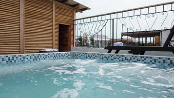 Una piscina con borde de azulejos, un edificio de madera con listones horizontales y una barandilla metálica con detalles decorativos.