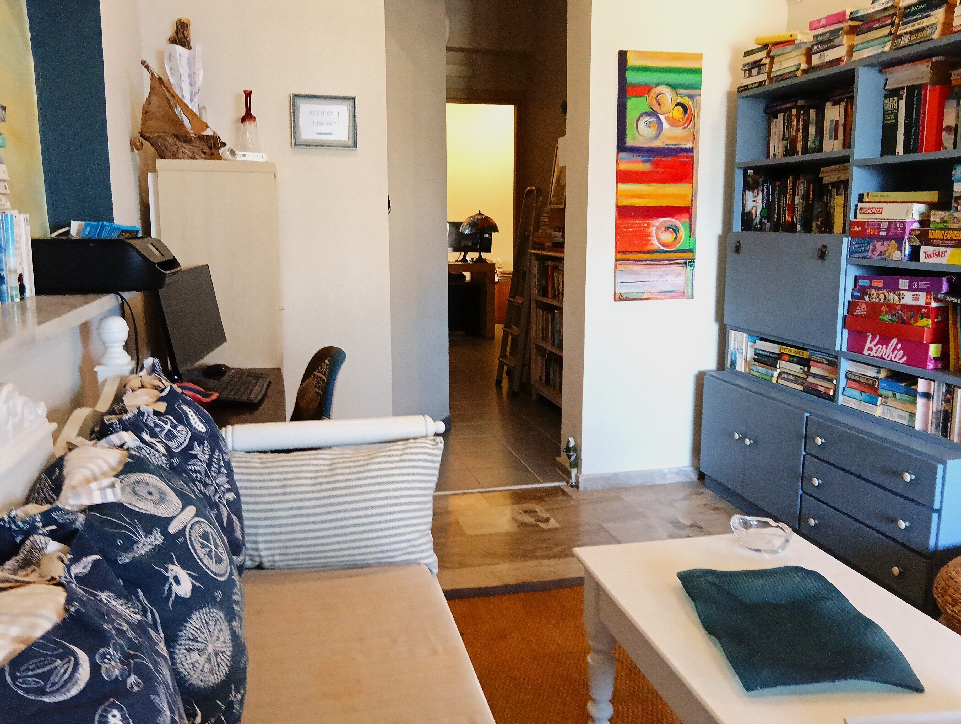 Una sala de estar con un sofá, una mesa de centro, una estantería y un escritorio con una computadora.