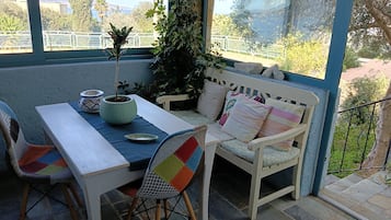 A sunlit patio with a table and chairs, a potted plant, and a bench with cushions.