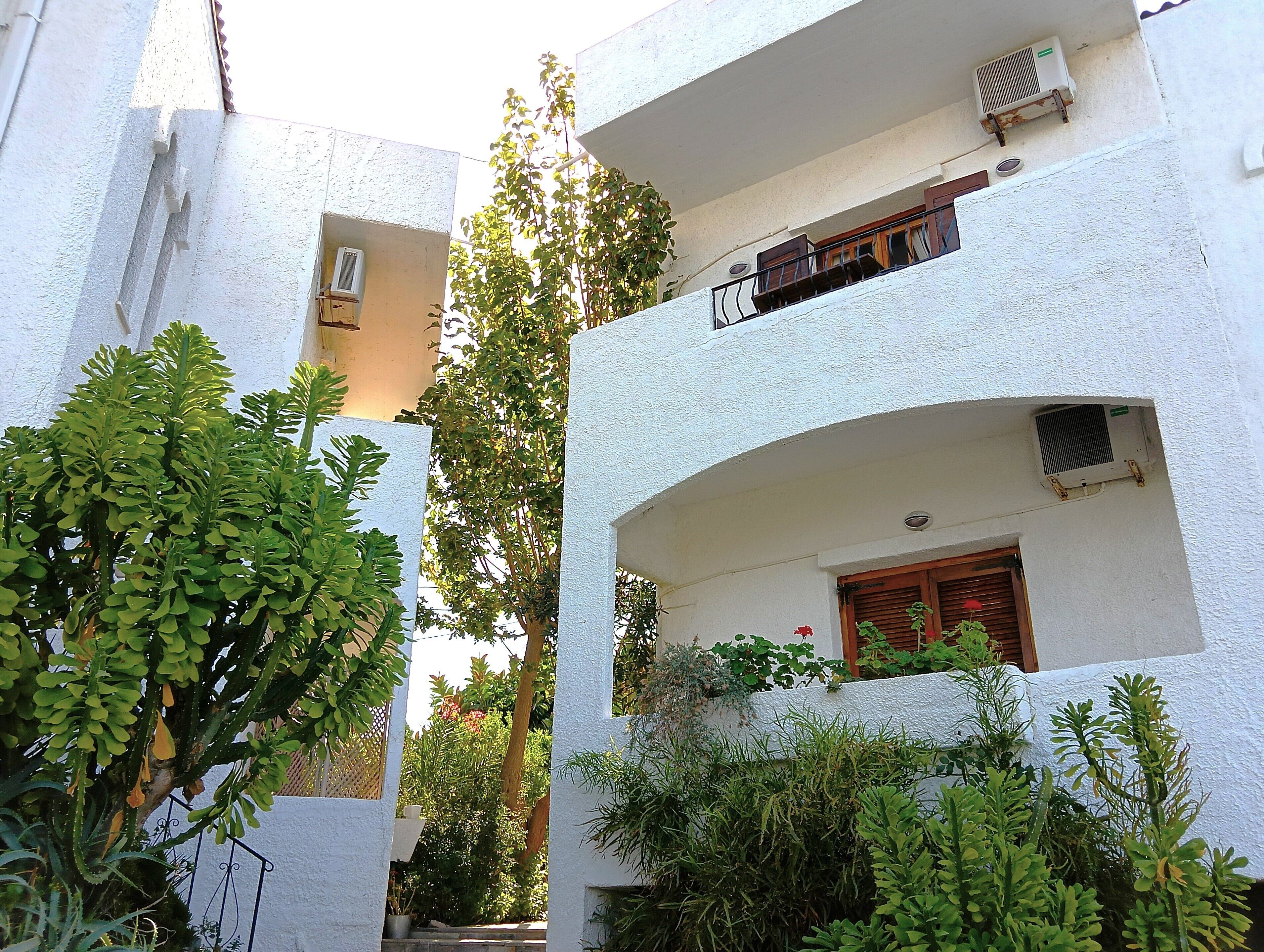 Un edificio de varios pisos con paredes exteriores blancas, balcones con barandillas y unidades de aire acondicionado.