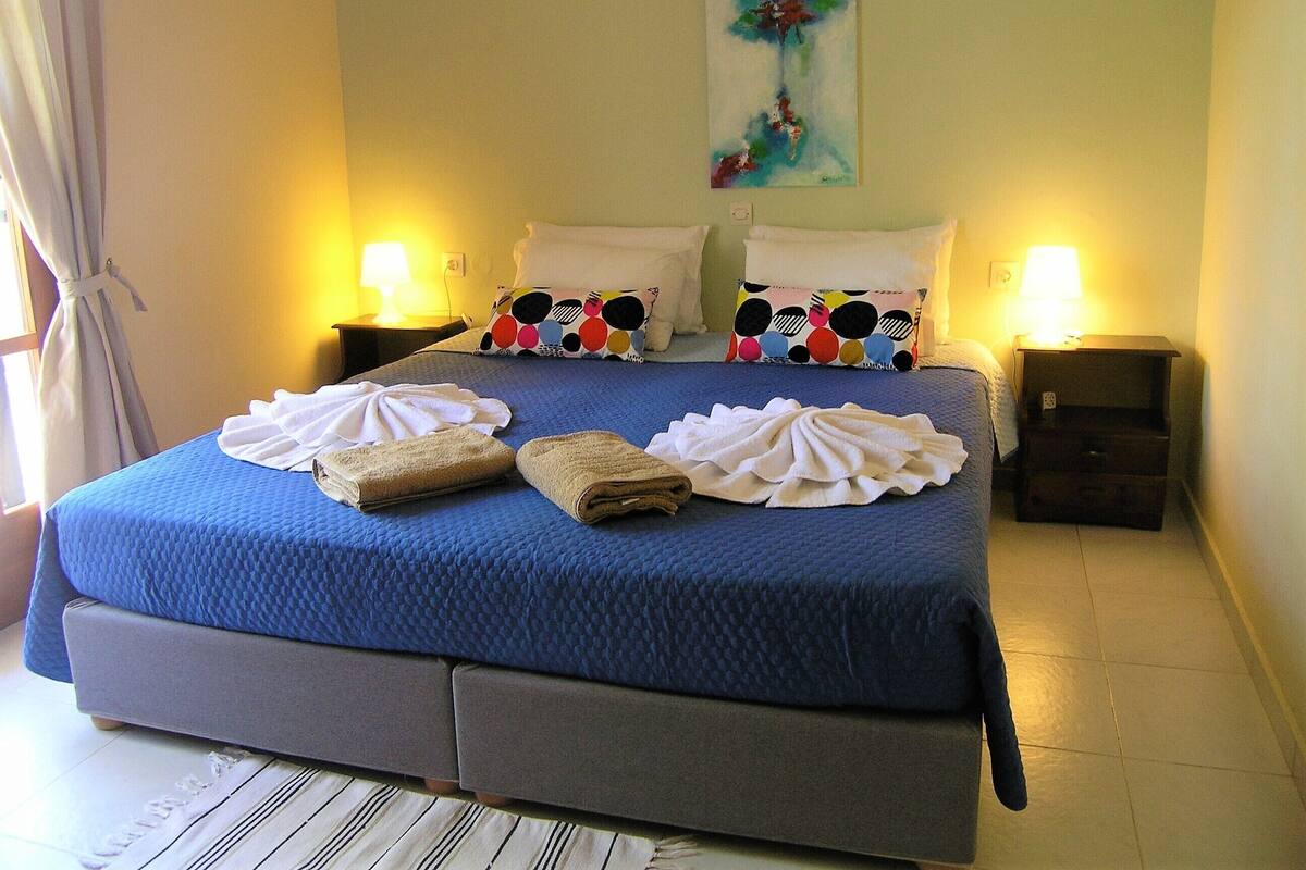 A hotel room with a large bed, two bedside tables with lamps, a painting on the wall, and towels on the bed.