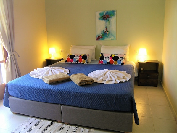 A hotel room with a large bed, two bedside tables with lamps, a painting on the wall, and towels on the bed.