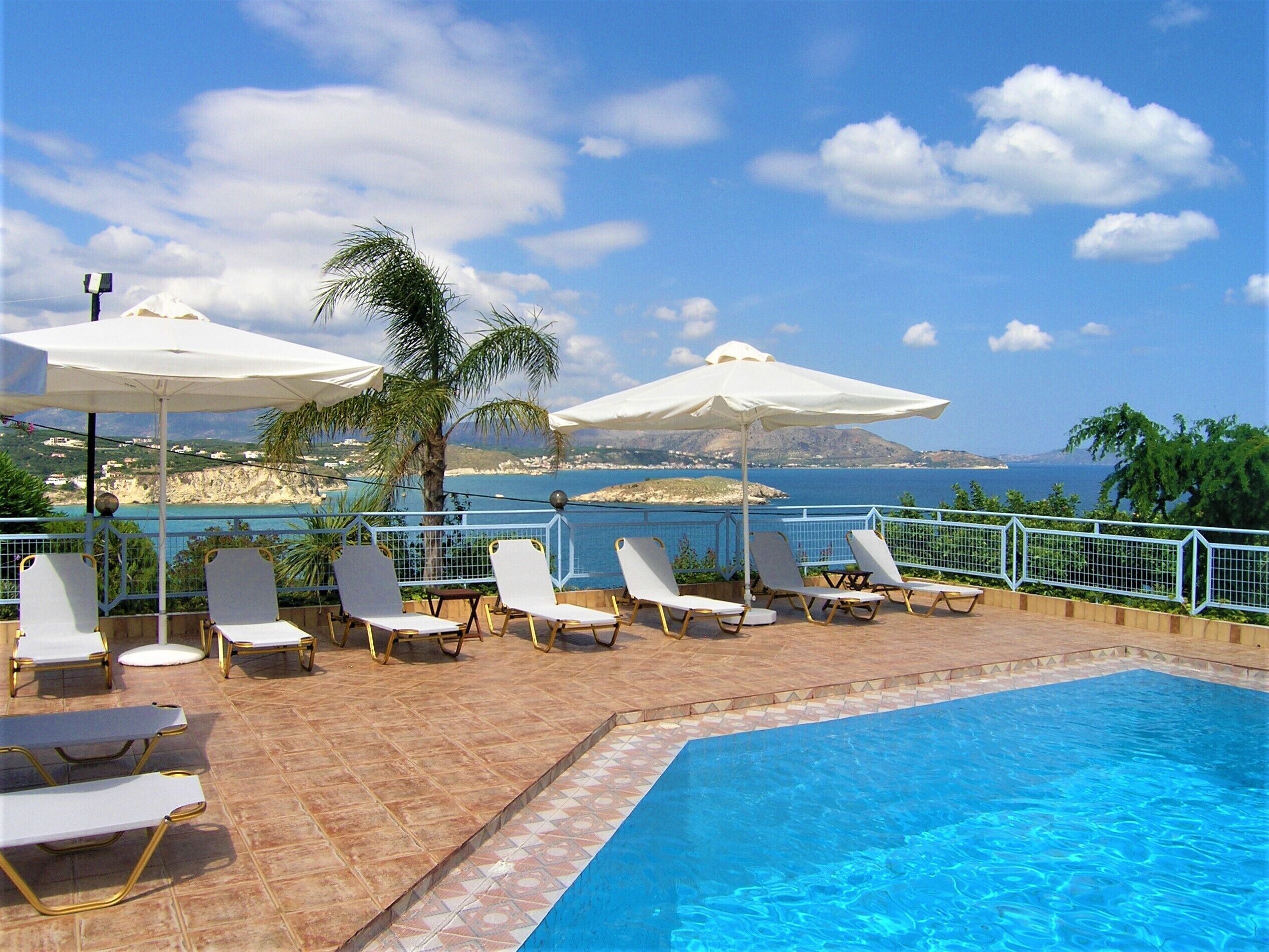 Zona junto a la piscina con sillones reclinables y sombrillas, con vistas a un paisaje costero.