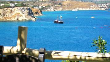 A coastal view with a wooden railing, a boat, and distant buildings on a hilly landscape.